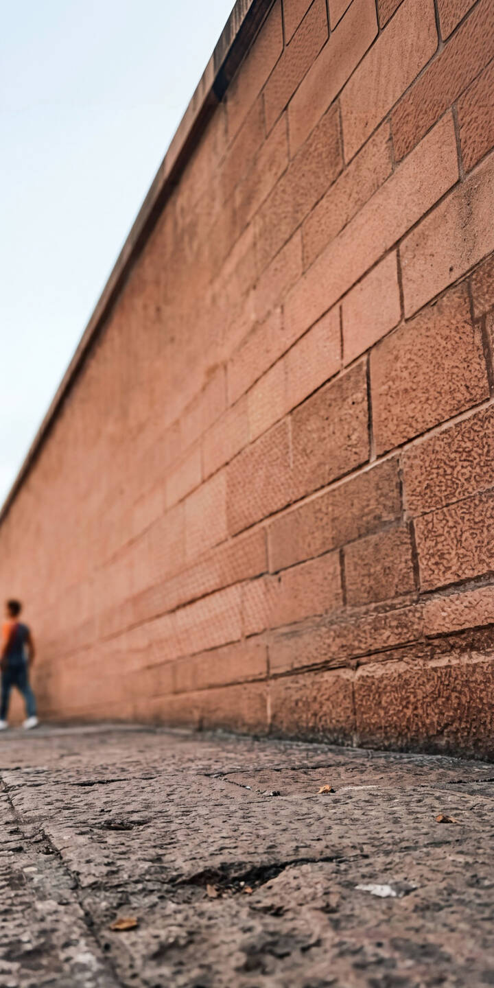 A breathtaking expanse of reddish-brown textured brick wall stretches into the distance under a pale sky in this stunning 4K wallpaper, featuring a solitary, out-of-focus figure walking along the ancient stone path; an ideal wallpaper for your iPhone. | architecture iphone minimalist wallpaper ancient texture mobile 4k wallpaper hd wallpaper perspective brick wall stone wall A breathtaking expanse of reddish-brown textured brick wall stretches into the distance under a pale sky in this stunning 4K wallpaper, featuring a solitary, out-of-focus figure walking along the ancient stone path; an ideal wallpaper for your iPhone.