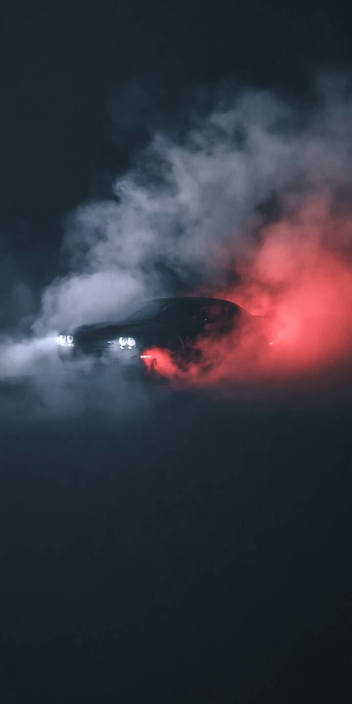 A dark performance car emerges through swirling smoke illuminated by intense red light. Bright headlights and dramatic shadows create a mysterious nighttime scene. | sports car dark headlights red smoke cinematic A dark performance car emerges through swirling smoke illuminated by intense red light. Bright headlights and dramatic shadows create a mysterious nighttime scene.