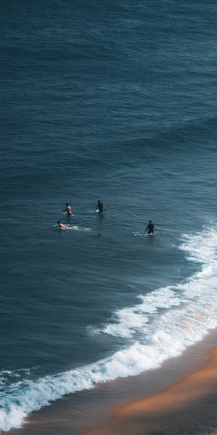 A small group of surfers waits in the deep blue ocean near a quiet shoreline. Gentle waves and warm coastal light capture a peaceful surfing moment. | beach ocean waves surfing coastal A small group of surfers waits in the deep blue ocean near a quiet shoreline. Gentle waves and warm coastal light capture a peaceful surfing moment.